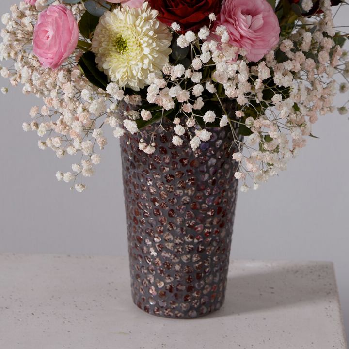 Floral arrangement in a textured vase on a light surface with a neutral background