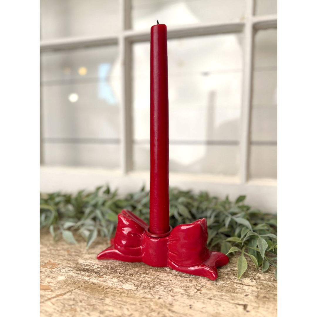 Red candle holder with a red candle on a wooden surface with greenery in the background