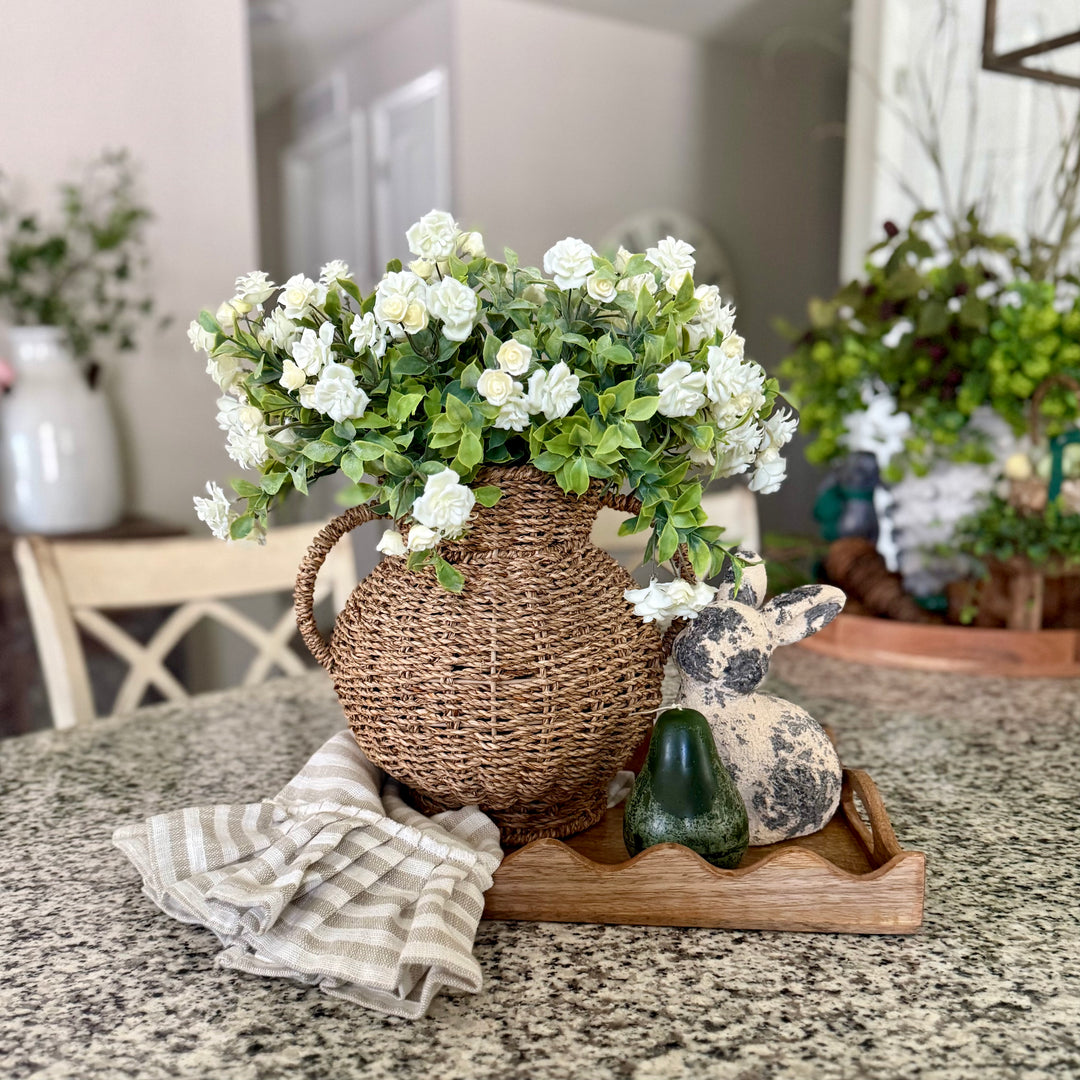 Decorative arrangement with a woven basket, flowers, and a stone rabbit on a table.