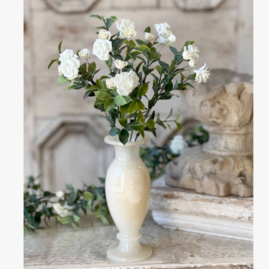 White flowers in a tall, slender vase on a rustic wooden surface with decorative elements.