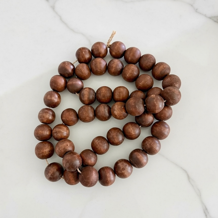A strand of medium brown wooden beads with a natural wood grain finish, coiled on a white marble surface.