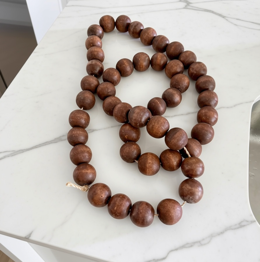 A strand of dark brown wooden beads, likely a prayer bead necklace or rosary, laid out on a white marble countertop.
