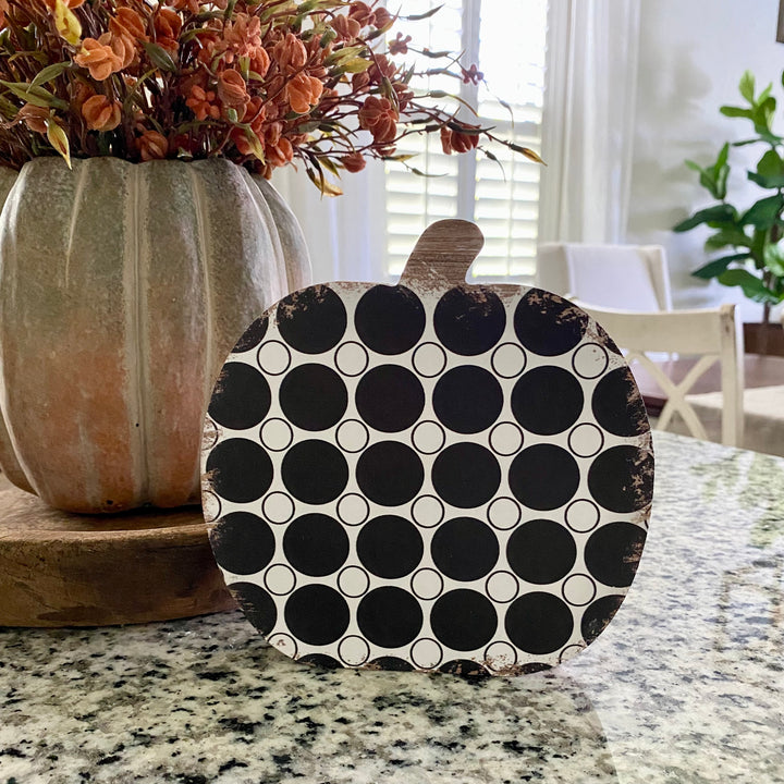 A wooden pumpkin sitter with a black and white polka dot pattern and a rustic finish, placed on a countertop.