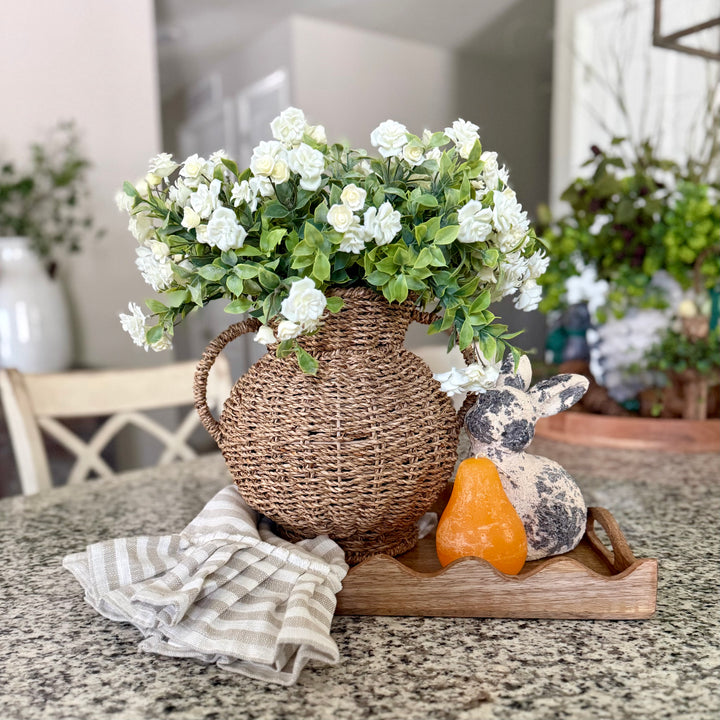 Decorative arrangement in a scallop mango wood tray with a seagrass vase, artificial white flowers, and bunny figurine on a table.