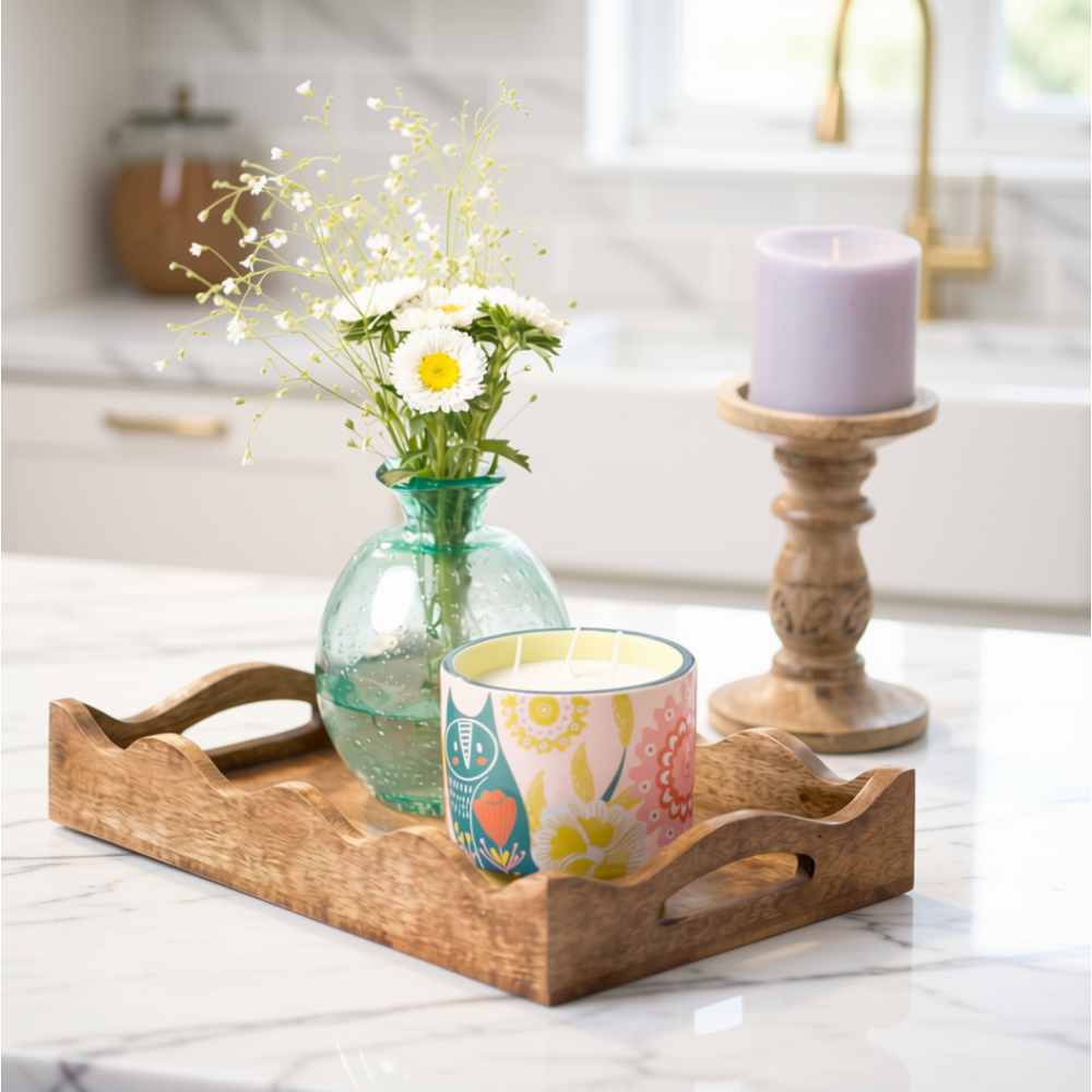 Wooden tray with a vase of flowers, colorful mug, and candle on a floral tablecloth.
