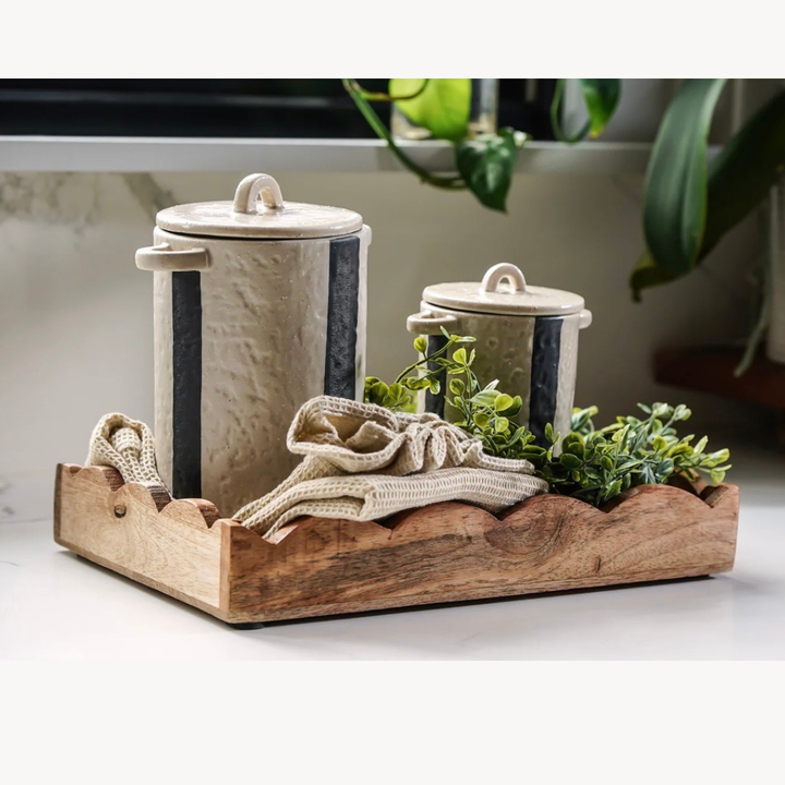 Decorative set with ceramic canisters, a wooden tray, and greenery on a light background