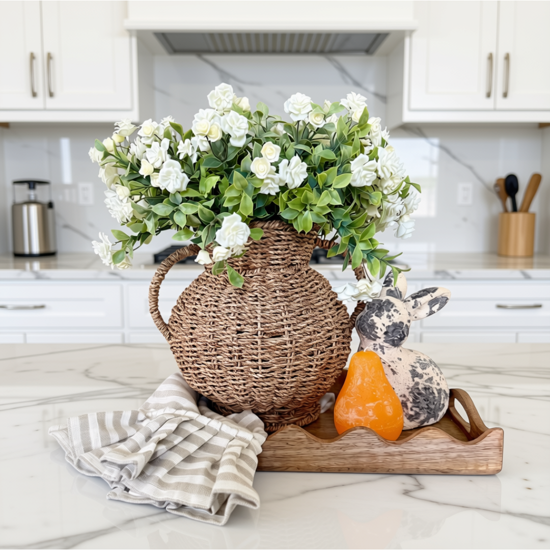 Decorative arrangement in a scallop mango wood tray with a seagrass vase, artificial white flowers, and bunny figurine on a table.