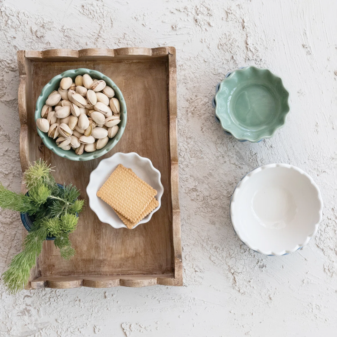 Wooden tray with a bowl of nuts, a plate of cookies, and a small plant on a light stone surface.