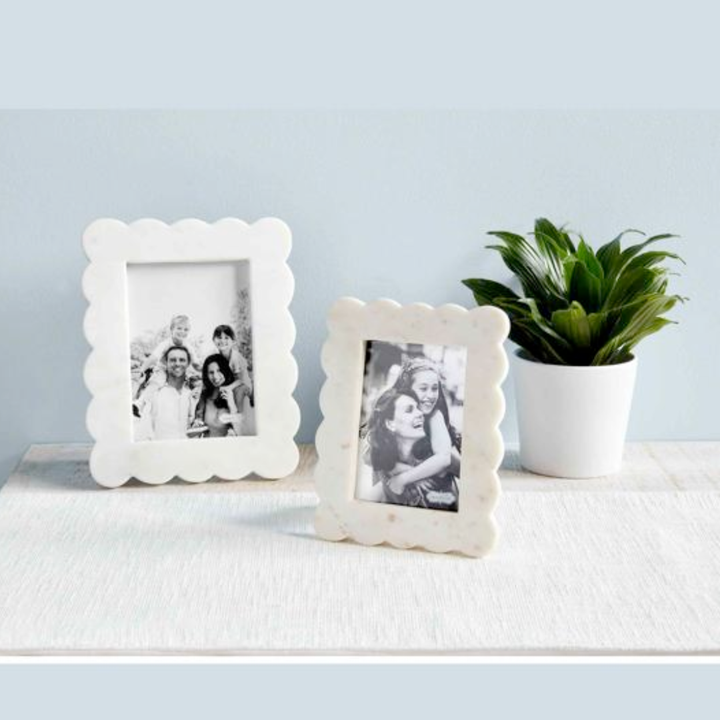 Two white scalloped photo frames with family pictures on a light blue wall background