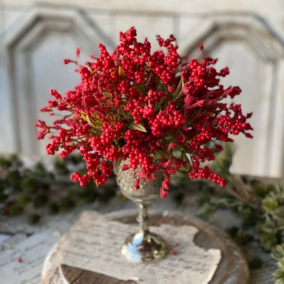 A decorative half sphere made of styrofoam with a arrangement of scarlet berries and tiny bubble berries on top, placed on a rustic wooden surface with a white background.