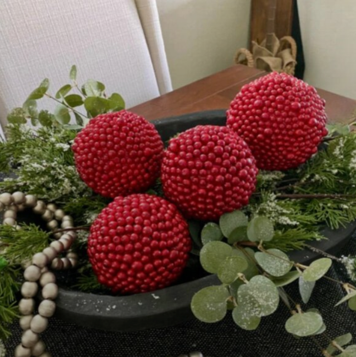 Decorative arrangement with red berry balls ornaments and greenery on a table.