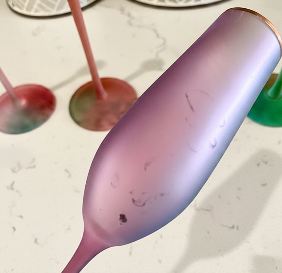 Close-up of a purple spoon on a marble surface with blurred colorful objects in the background