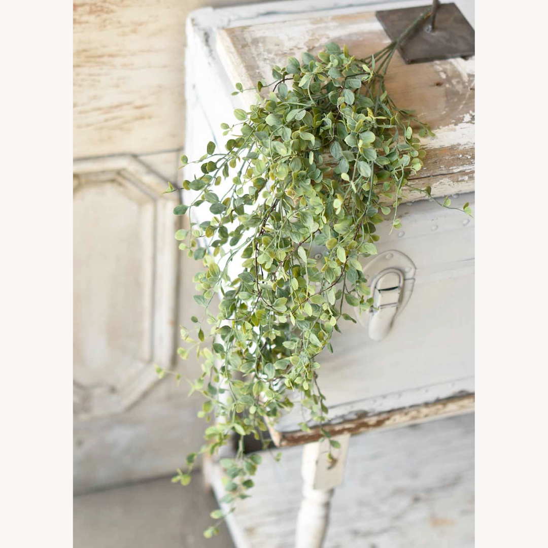 Artificial eucalyptus leaves hanging from a wooden frame against a neutral background