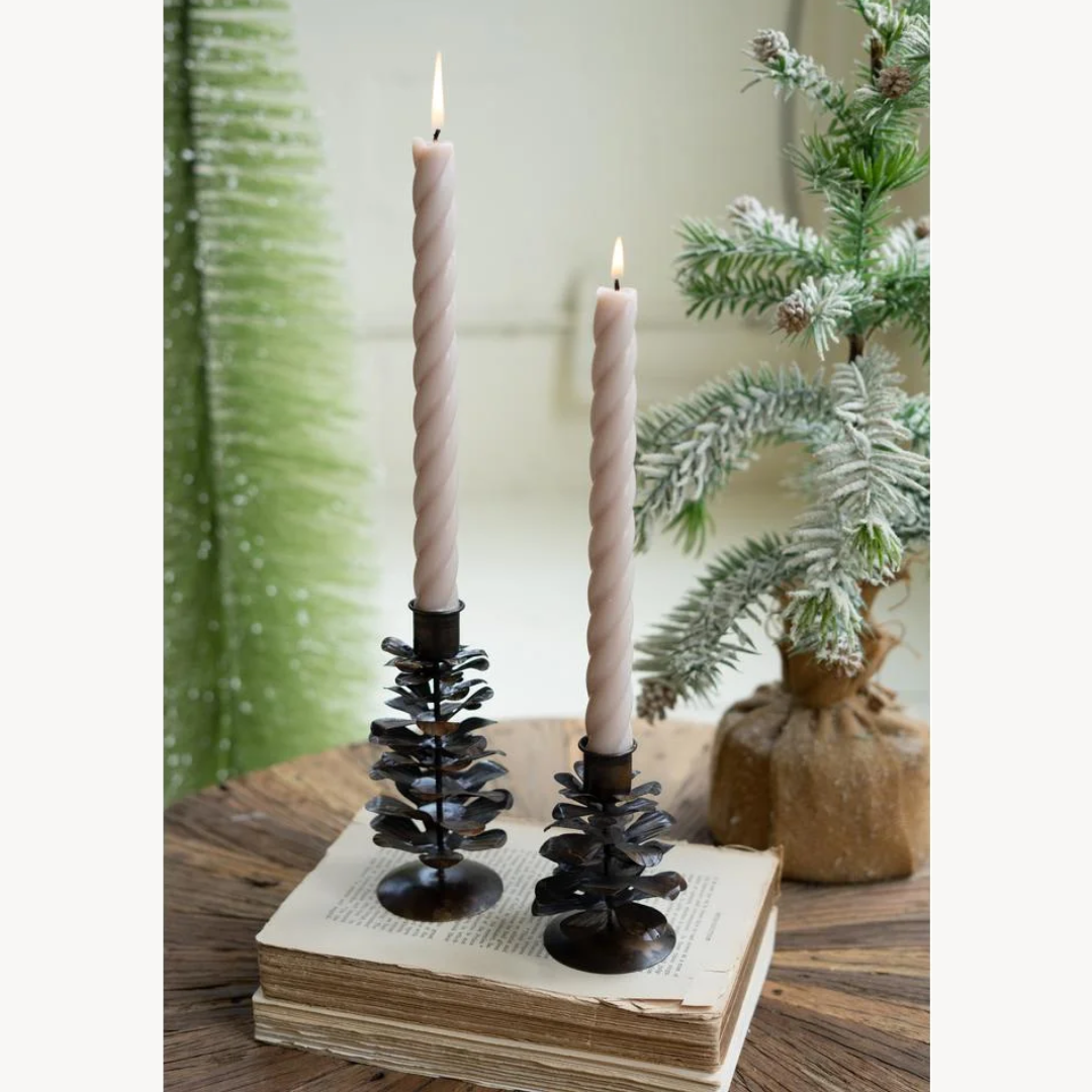 Decorative candle holders with candles on a stack of books, surrounded by greenery.