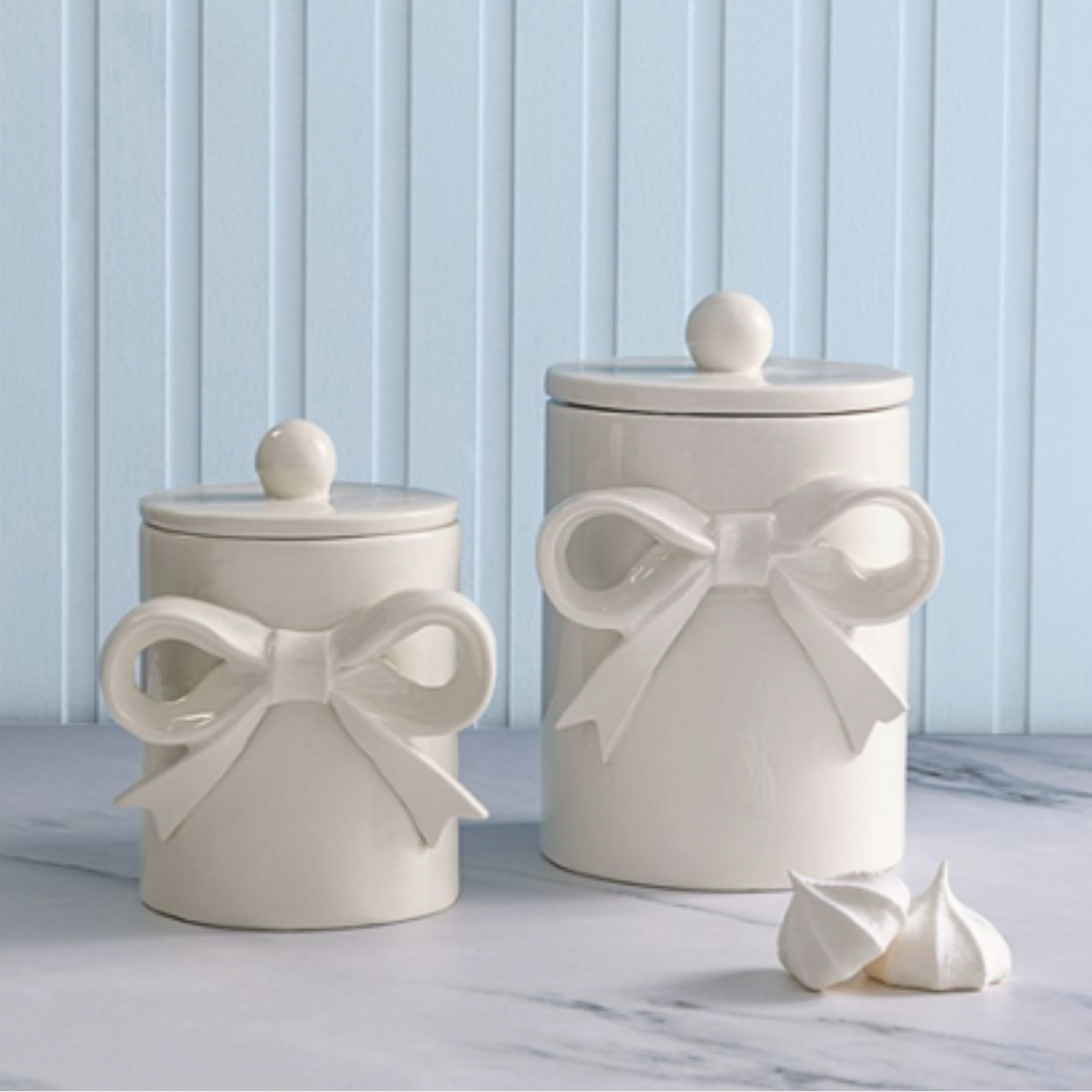 Two white ceramic jar canisters with bow designs on a light blue background