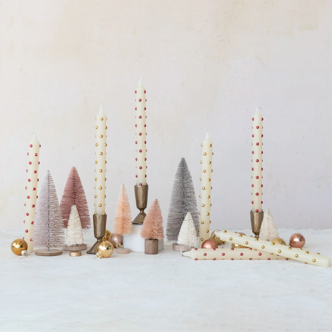 Decorative setup with candles, small trees, and ornaments on a white surface.