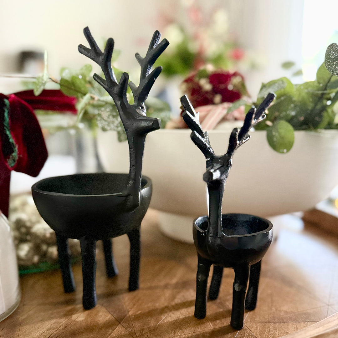 Two black deer-shaped bowls on a wooden surface with a blurred indoor background.