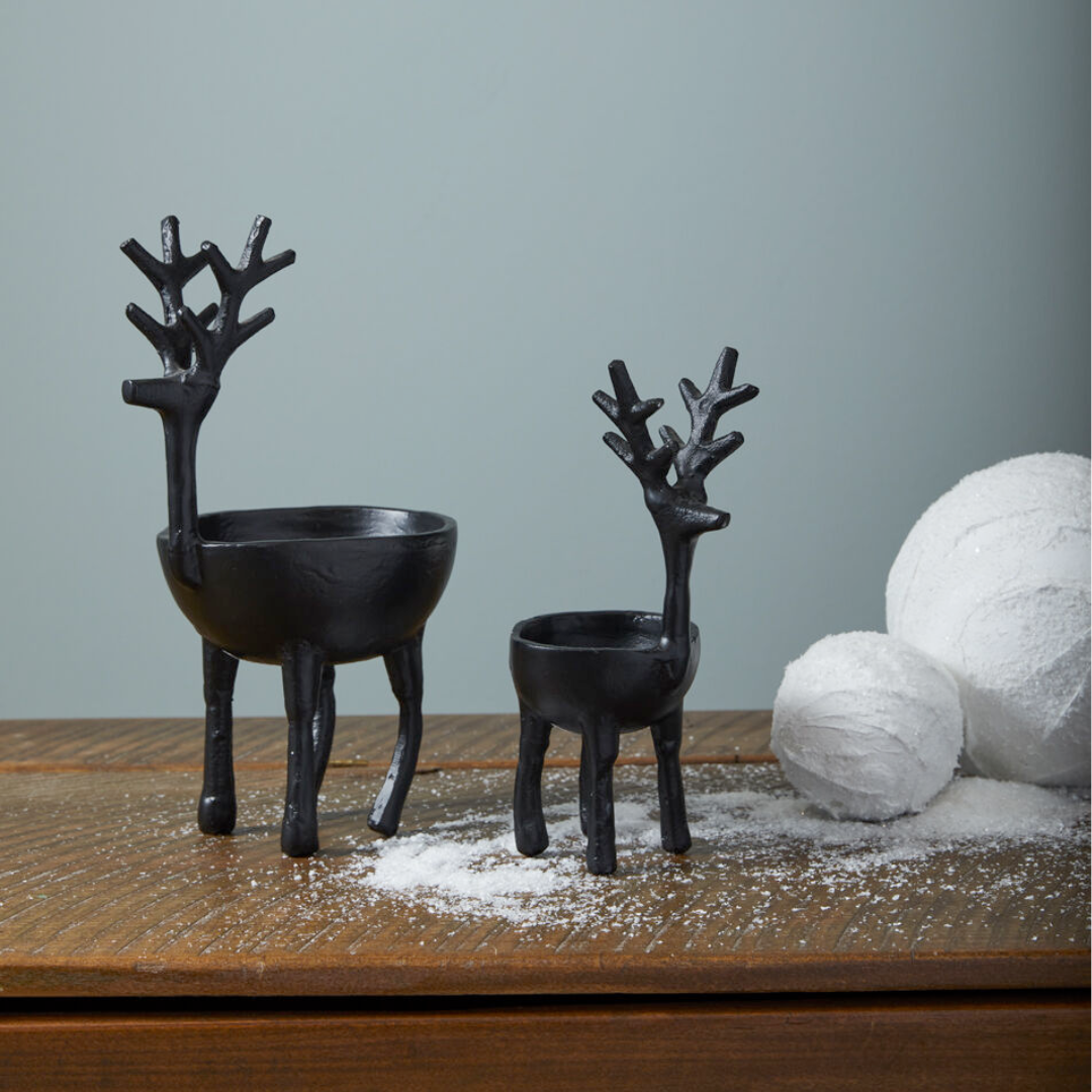 Two black deer-shaped bowls on a wooden surface with decorative snowballs.