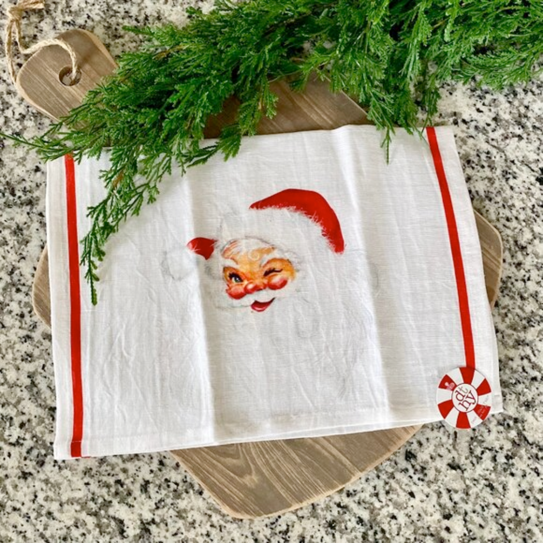Dish towel with Santa Claus face design on a granite surface with greenery.