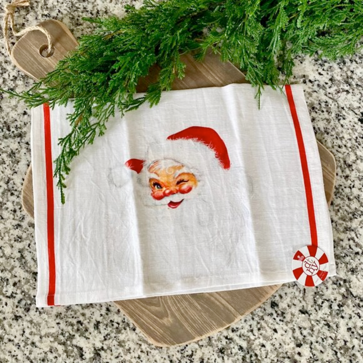Dish towel with Santa Claus face design on a granite surface with greenery.