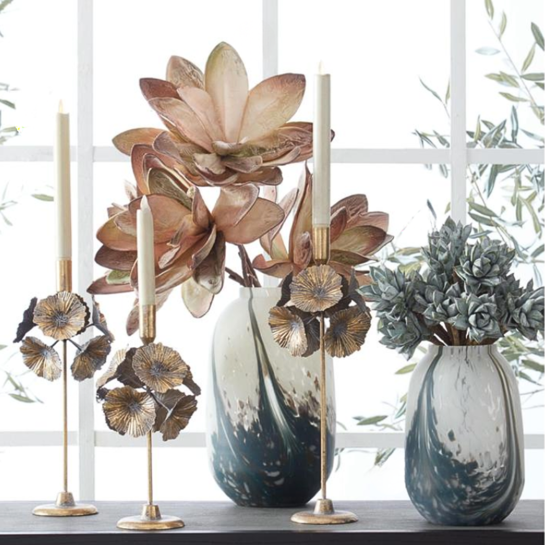 Decorative flower arrangements with vases and candle holders on a console table