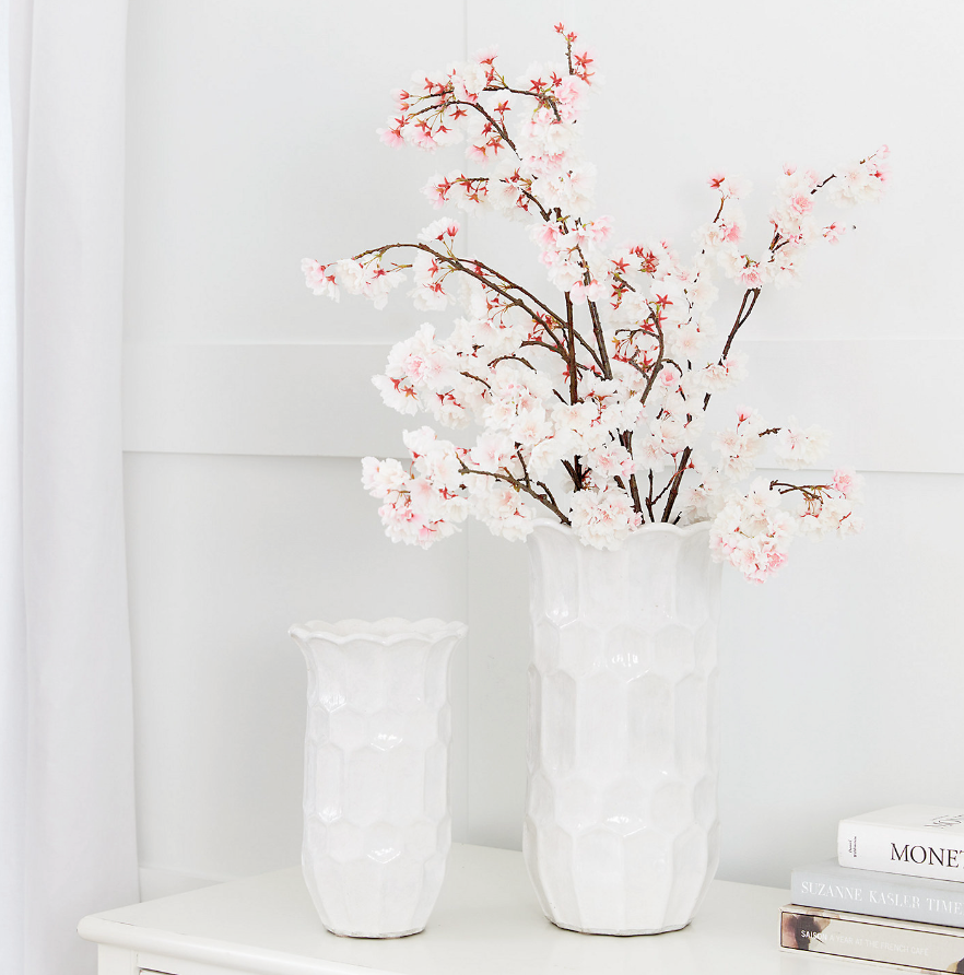 Two white vases with cherry blossom branches on a white surface.
