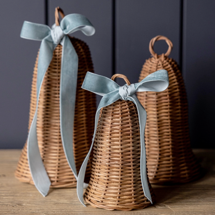 Three rattan bells with ribbons on a wooden surface against a dark background