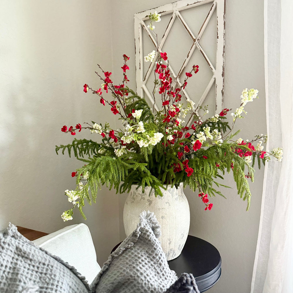 Floral arrangement in a white vase on a black table with a decorative windowpane panel in the background.