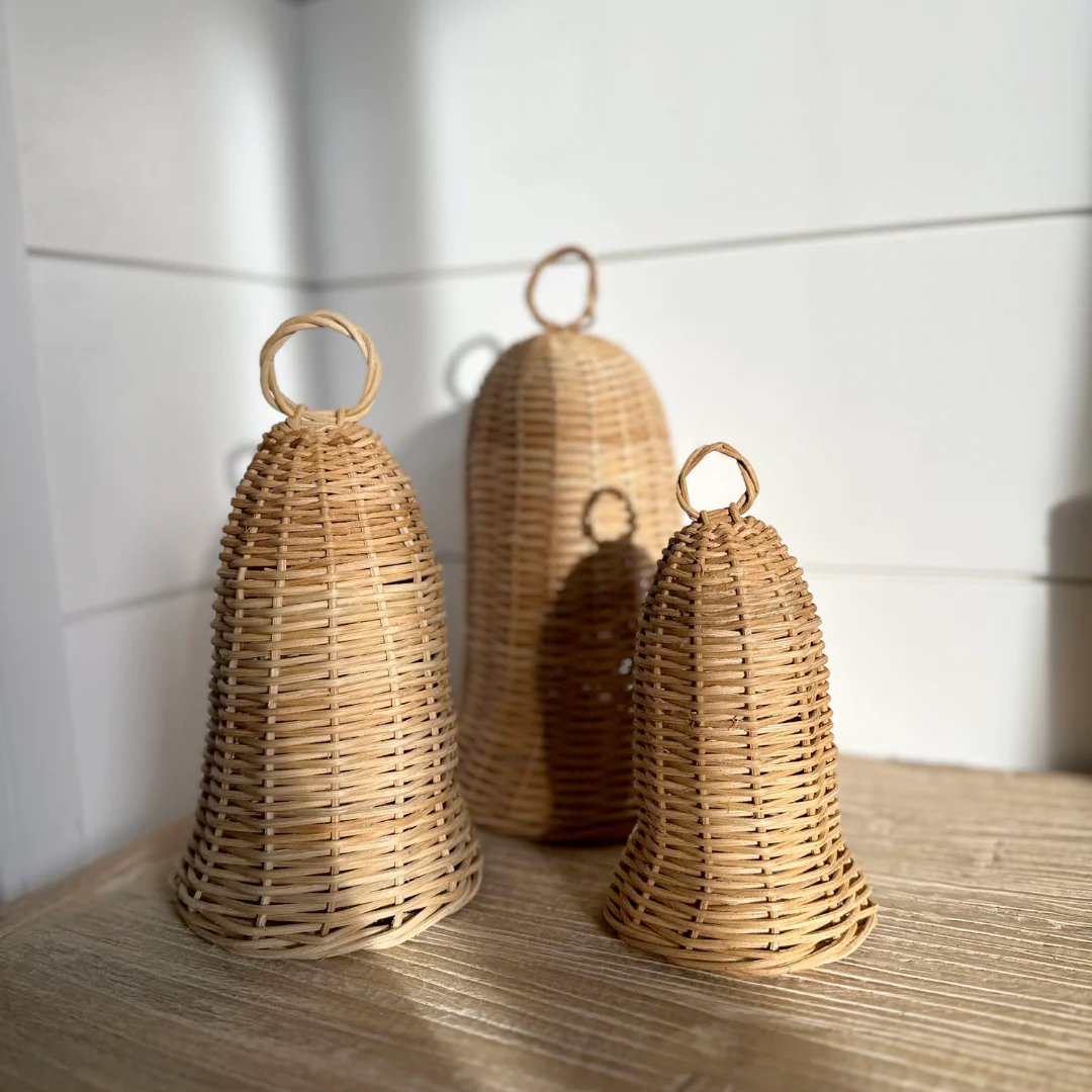 Three woven rattan bells on a wooden surface with a white tiled wall background