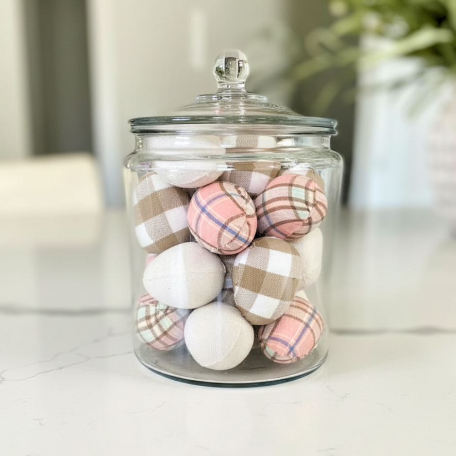 Glass jar with checkered and solid Easter eggs on a white surface
