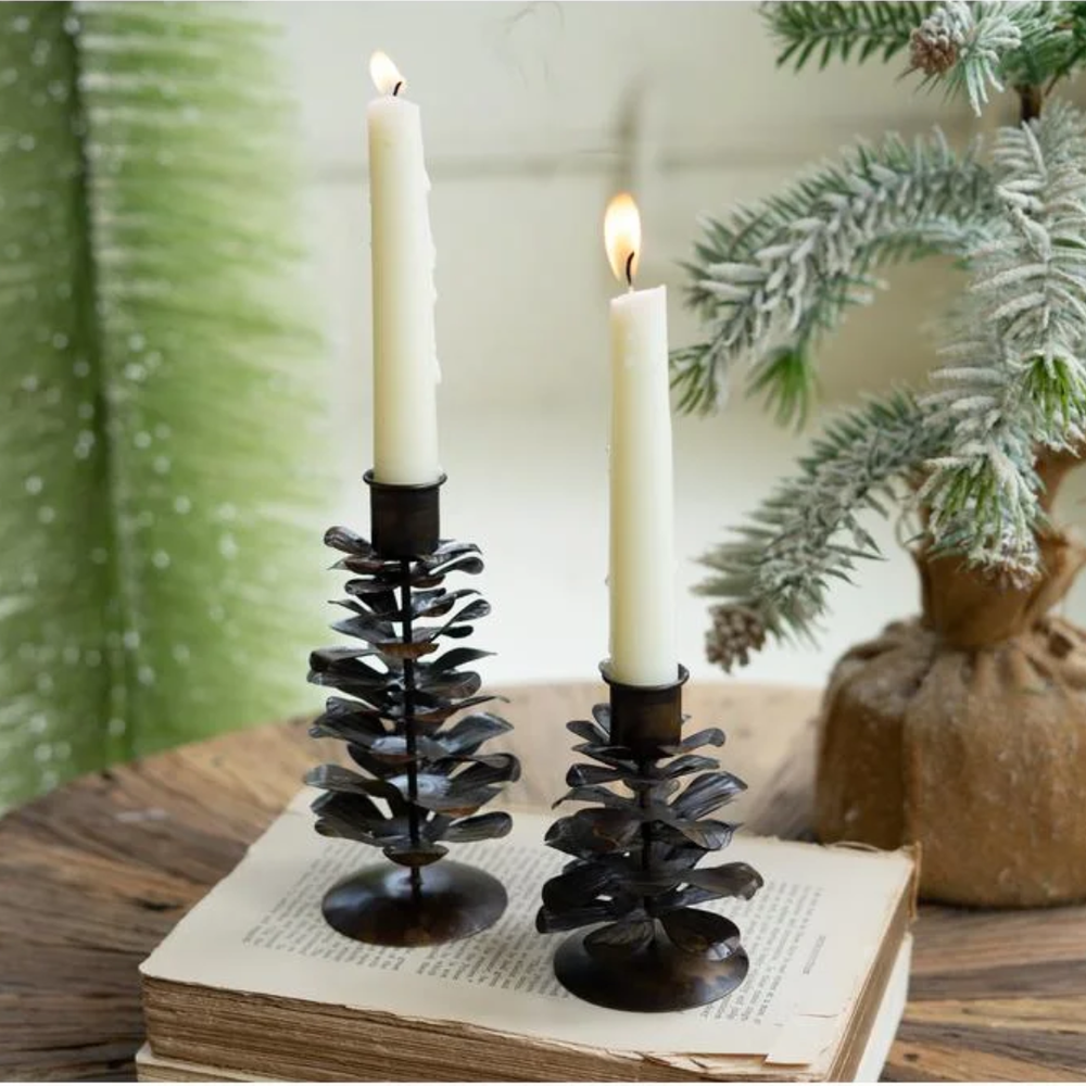 Two black metal candle holders with lit candles on an open book, with a Christmas tree and decorations in the background.