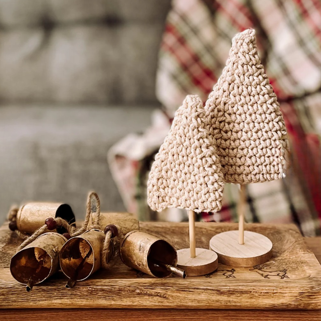 Crocheted Christmas trees and bells on a wooden surface with a blurred background