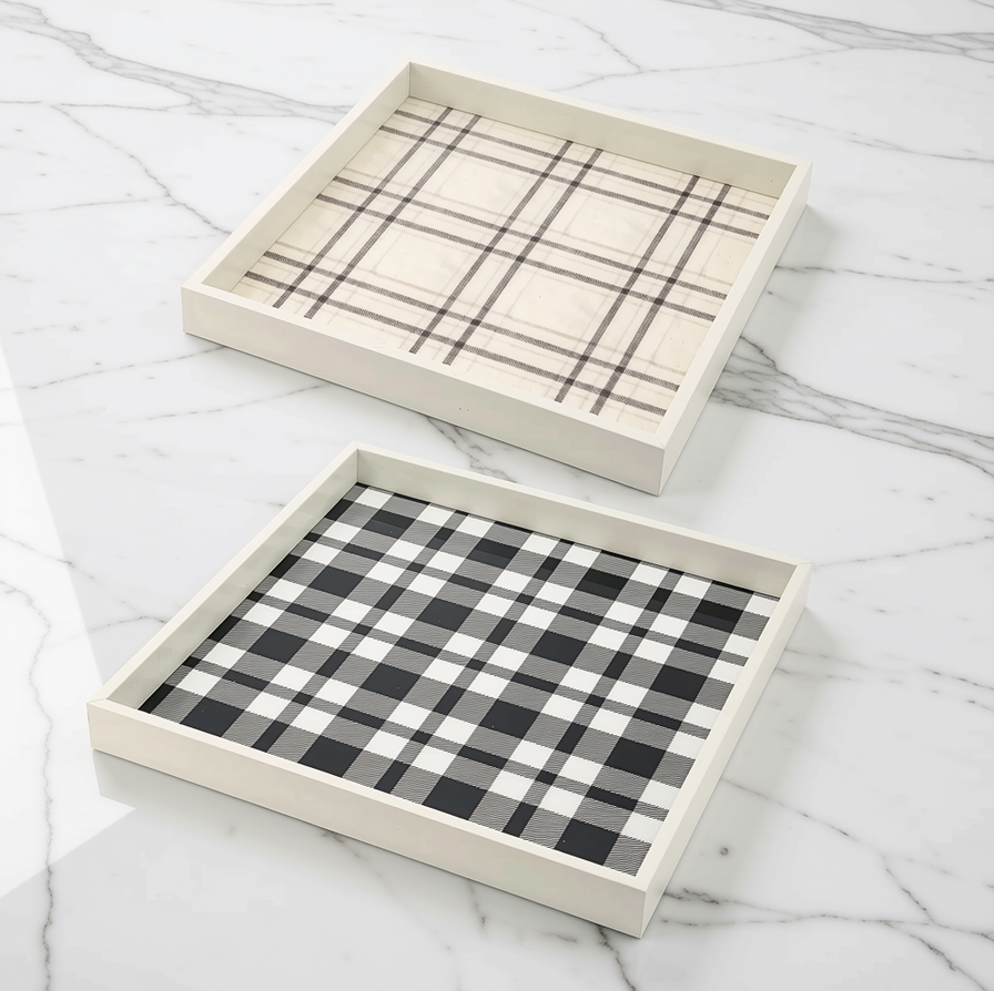Two rectangular decorative trays with white wooden frames, one with a beige plaid pattern and the other with a black and white buffalo plaid pattern, displayed on a white marble surface.