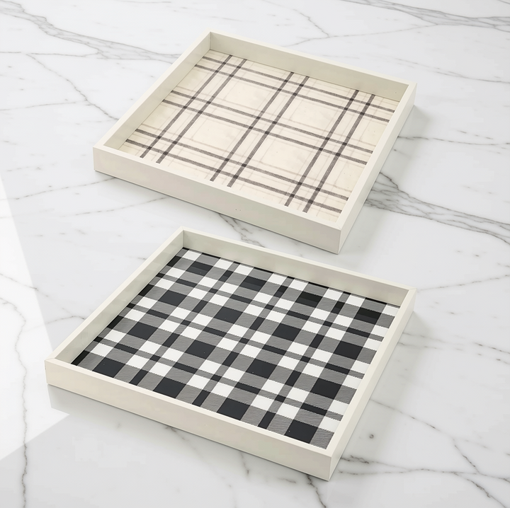Two rectangular decorative trays with white wooden frames, one with a beige plaid pattern and the other with a black and white buffalo plaid pattern, displayed on a white marble surface.