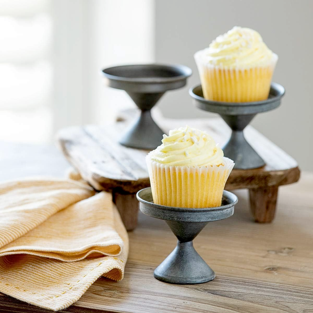 Yellow cupcakes on small metal stands on a wooden surface with a beige towel.