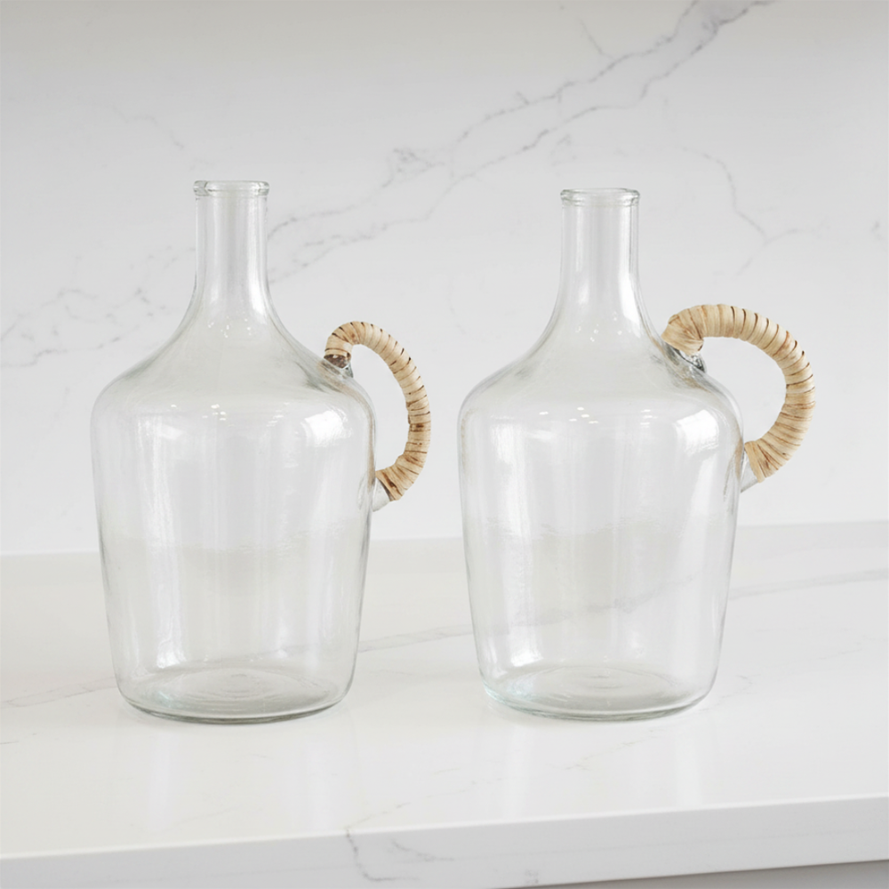 Two clear glass jugs with woven handles on a white surface.