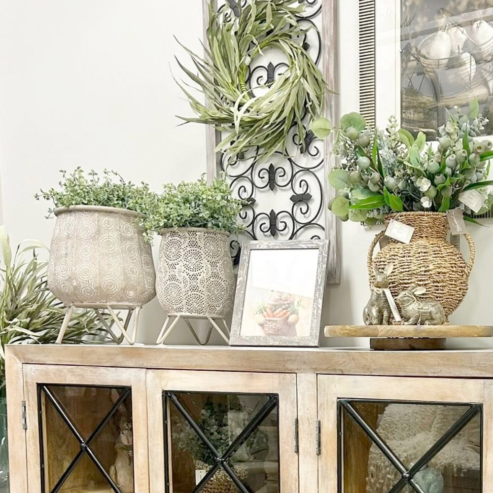 Decorative setting with plants, a wreath, and framed picture on a wooden cabinet.
