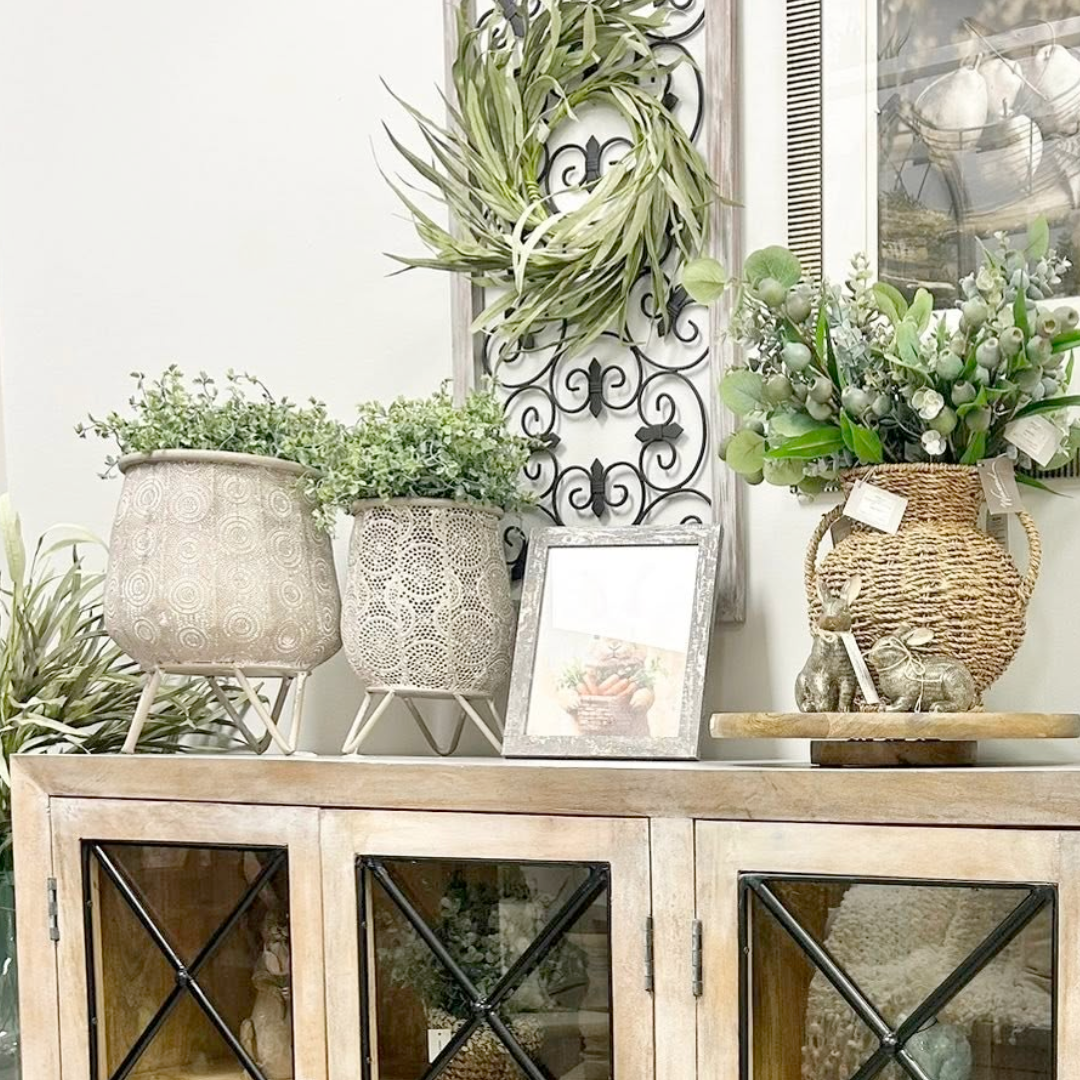 Decorative setting with plants, a wreath, and framed picture on a wooden cabinet.