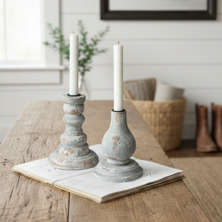 Two rustic candle holders with candles on a wooden table.