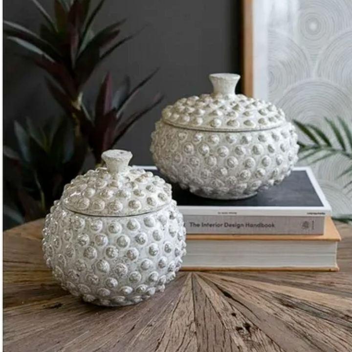 Two textured white ceramic containers on a wooden surface with books underneath.