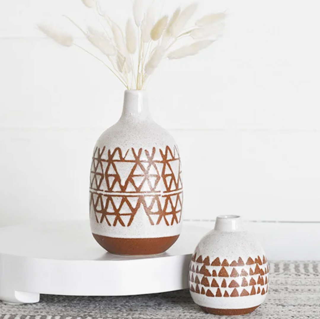 Two terracotta vases with geometric patterns, one larger than the other, against a white background with decorative dry plants inside the larger vase.