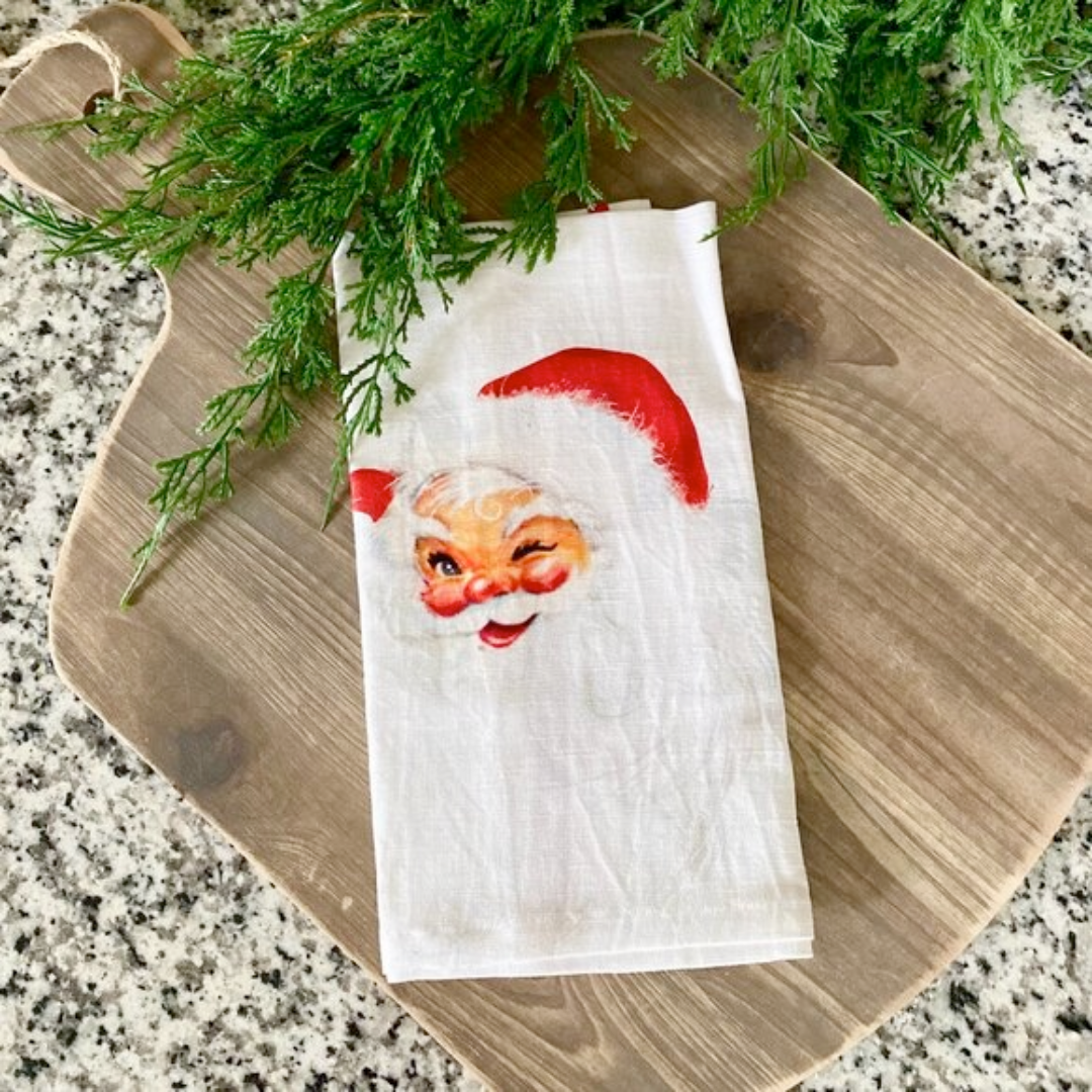 Napkin with Santa Claus face design on a wooden cutting board with greenery