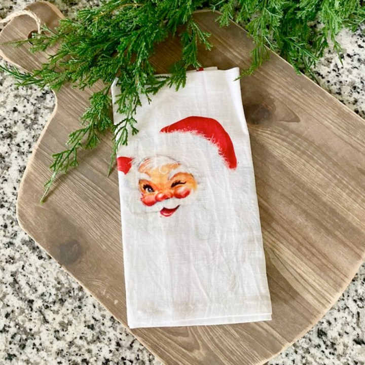 Napkin with Santa Claus face design on a wooden cutting board with greenery