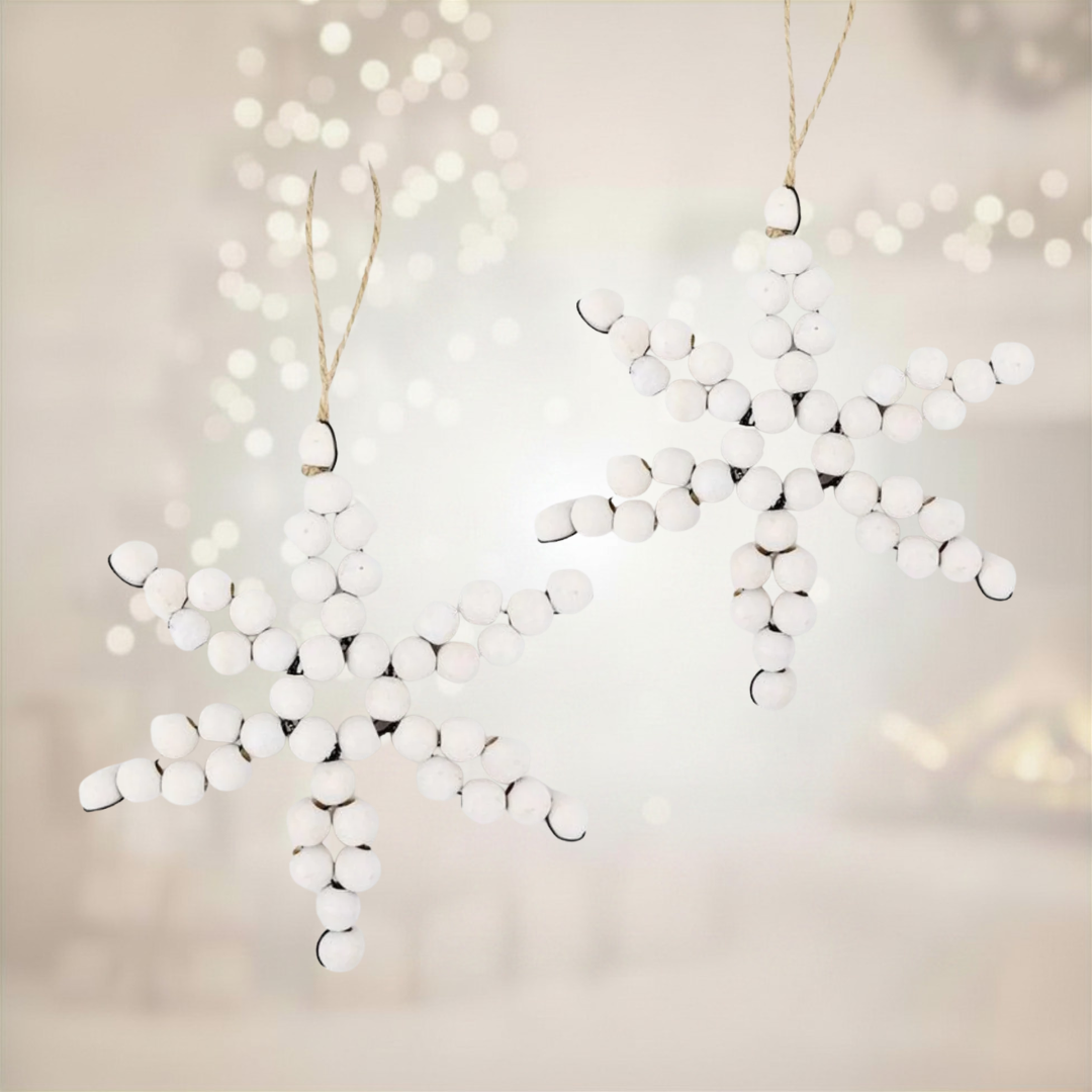 White snowflake-shaped ornaments hanging against a soft, blurred background with lights.