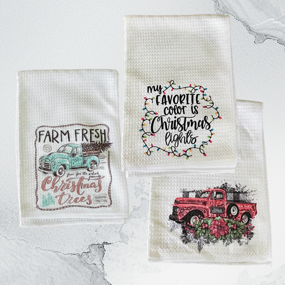Three decorative towels with Christmas-themed designs on a marble surface.