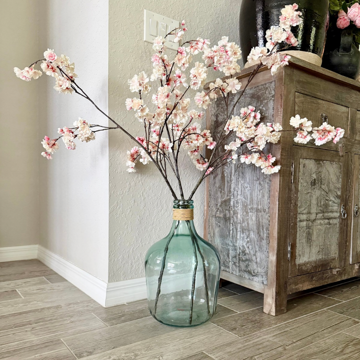Decorative vase with cherry blossom branches on a wooden floor next to a rustic cabinet.