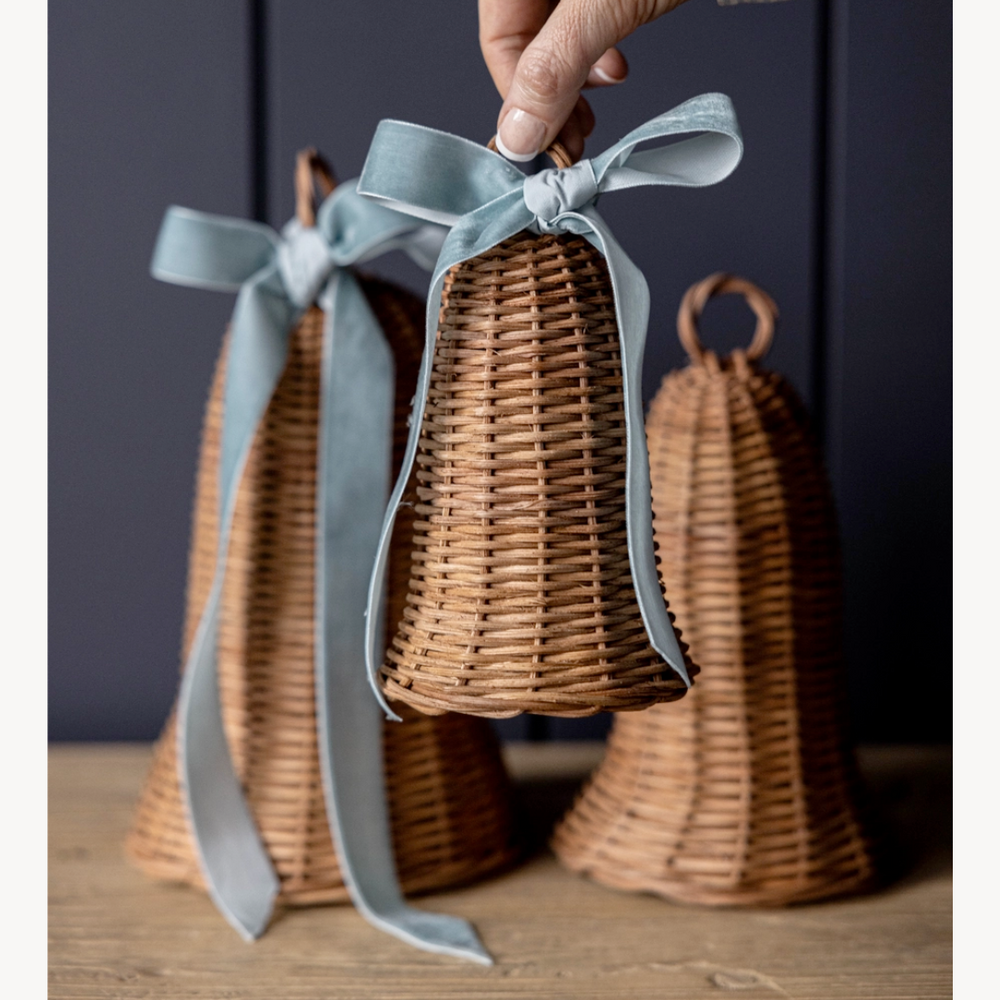Rattan bell-shaped containers with blue ribbons on a wooden surface against a dark background