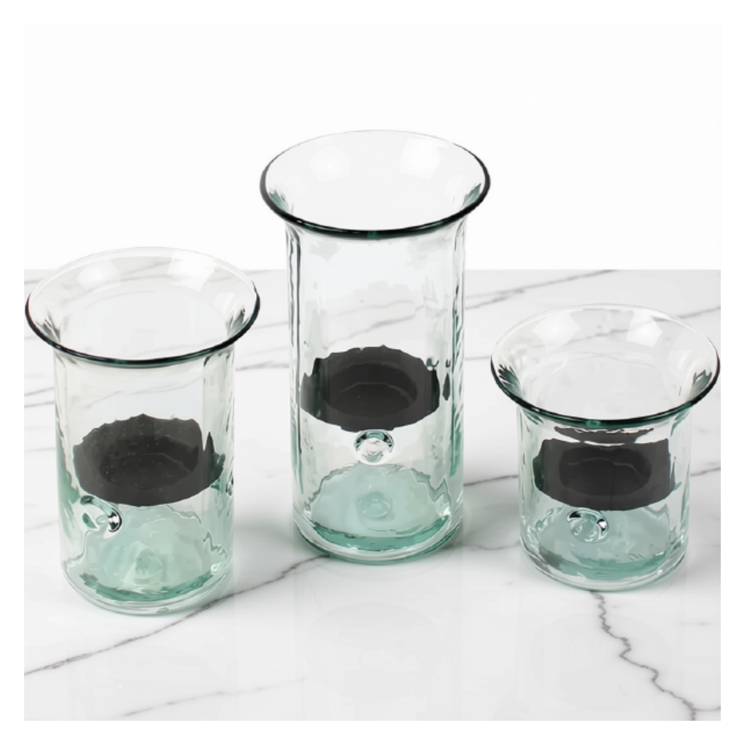 Three clear glass candle holders with a dark gray inner ring and a light green tinted outer base, arranged on a white marble surface against a white background.