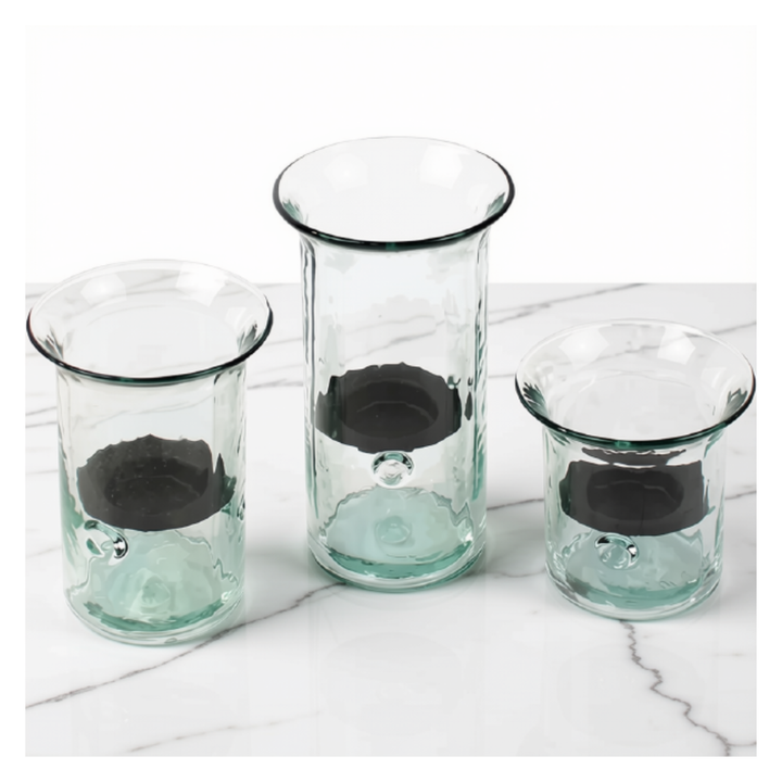 Three clear glass candle holders with a dark gray inner ring and a light green tinted outer base, arranged on a white marble surface against a white background.