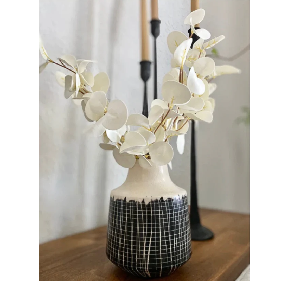 Decorative vase with black and white pattern on a wooden surface, featuring white eucalyptus flowers.